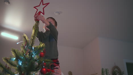 Set-the-final-decoration-for-the-Christmas-tree.-A-boy-places-a-star-on-top-of-a-Christmas-tree.-High-quality-4k-footage